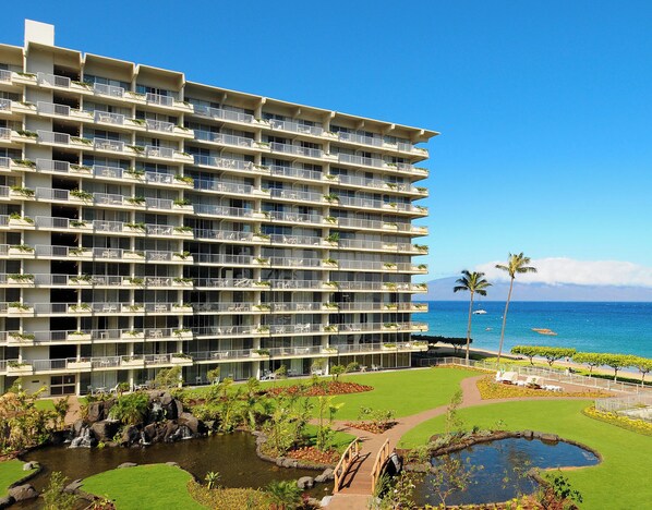 Modern beachfront property featuring private balconies, landscaped gardens with koi ponds, and stunning ocean views with palm trees along the shore. - Ocean Views | Aston Whaler at Kaanapali 0770 – Pool, Hot Tub & Spa (Lahaina)