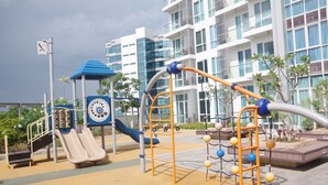 Un parque infantil con toboganes y estructuras para escalar, rodeado por un edificio con ventanas y balcones grandes.