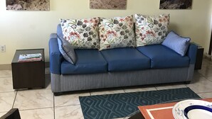 Una sala de estar con un sofá azul, cojines estampados y tres cuadros con paisajes playeros en la pared.