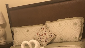 Habitación de hotel con una cama, cubrecama y almohadas con estampado floral, incluyendo una toalla dispuesta en forma de corazón.
