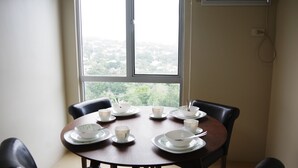Mesa de comedor con cuencos y tazas, ubicada cerca de una ventana con vistas a un paisaje urbano.