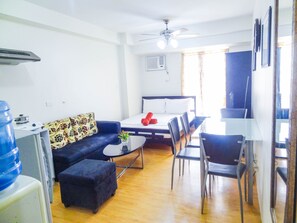 A compact hotel room with a bed, a sofa, a dining table, and chairs.