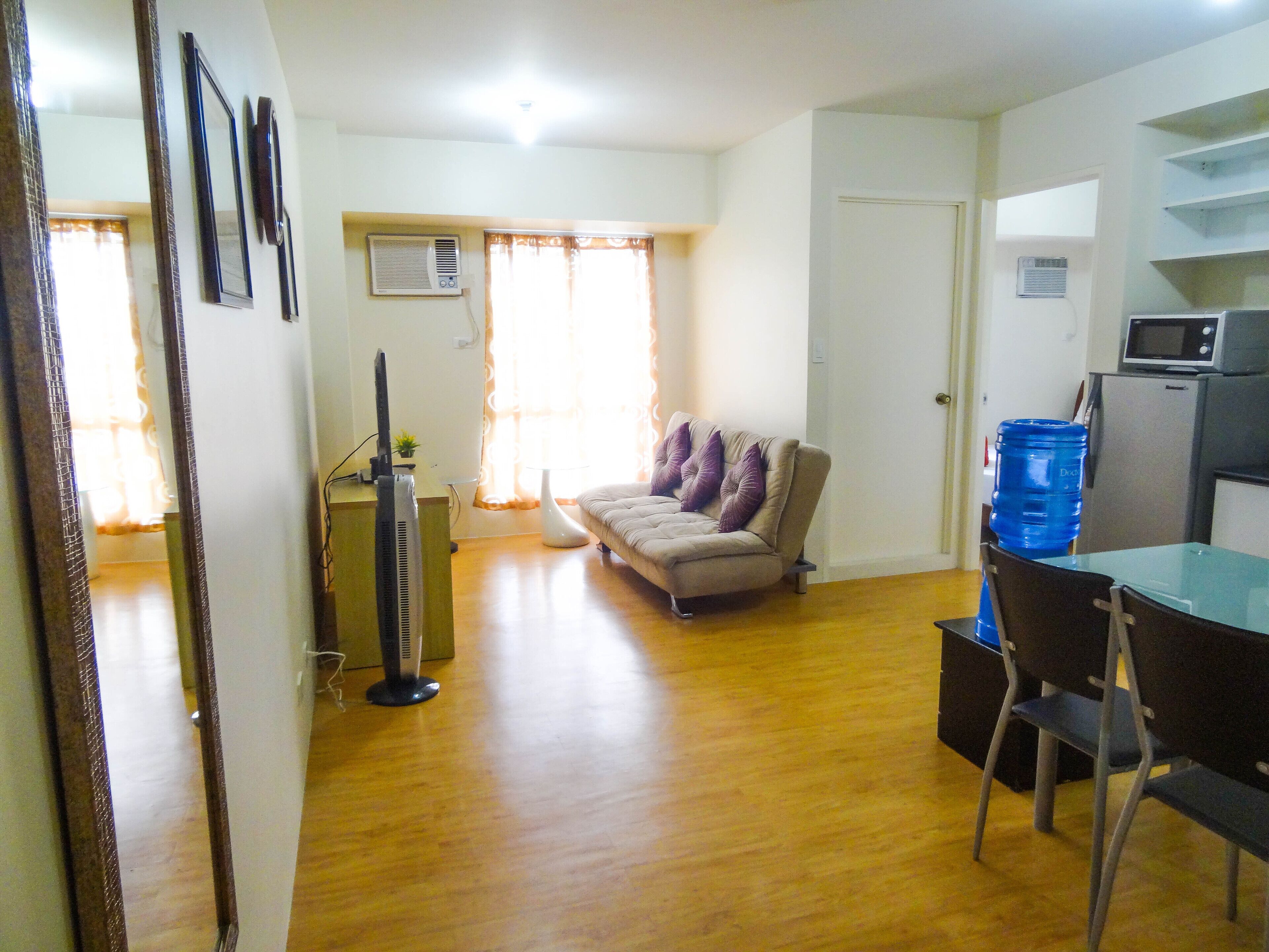 Un soggiorno con divano, un tavolo da pranzo con sedie, angolo cottura con forno a microonde e dispenser d'acqua.