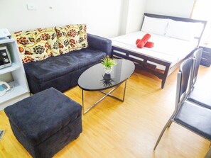 Una habitación moderna con sofá, una mesita con planta, cama con toallas enrolladas y una silla.
