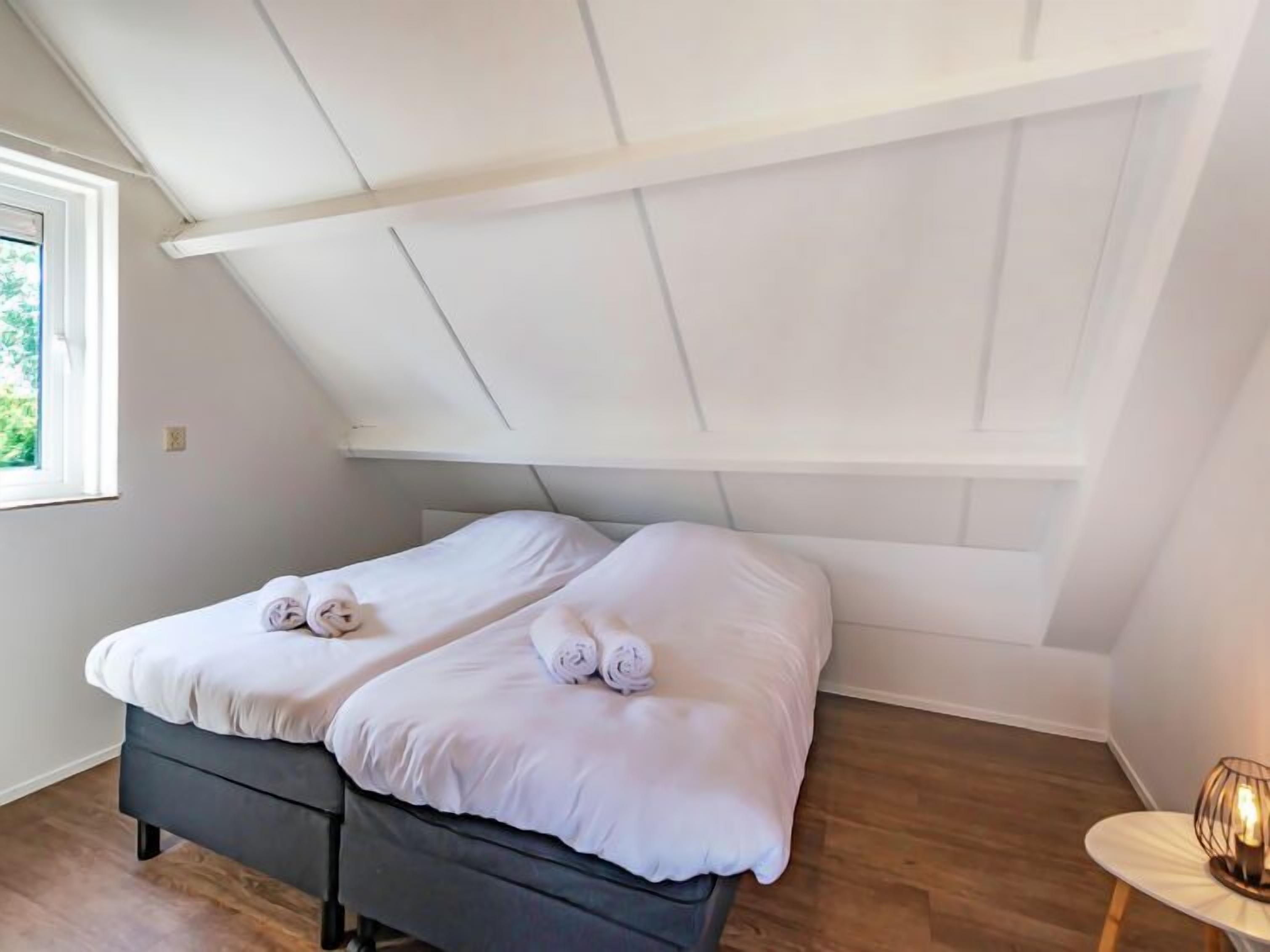 Un lit simple avec du linge de lit blanc et des serviettes enroulées, un plancher en bois et un plafond en pente.