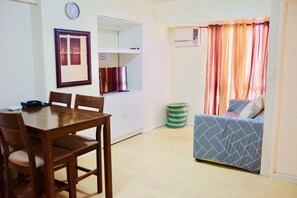 Un espacio habitable compacto con zona de comedor, kitchenette y una cama con cortinas.
