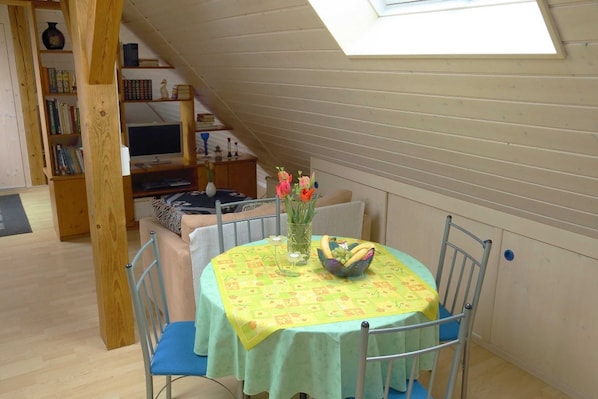 A dining area with a table set for two, a bookshelf, and a skylight.