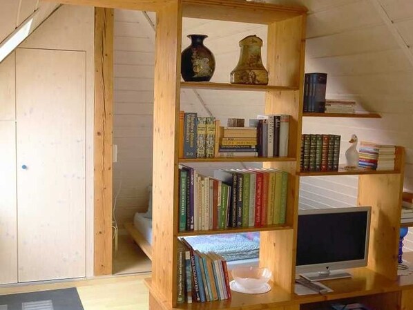 Una estantería de madera con libros y adornos, un televisor y un escritorio de madera.