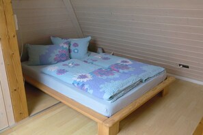 Ein Einzelbett mit floralem Überwurf in einem Raum mit Holzwänden und Holzboden.
