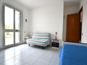 A bedroom with a bed, a chair, a nightstand, a lamp, and a door.