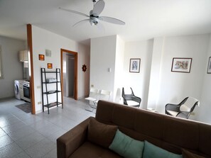 A living room with a brown sofa, a ceiling fan, a washing machine, and a dining area with chairs.