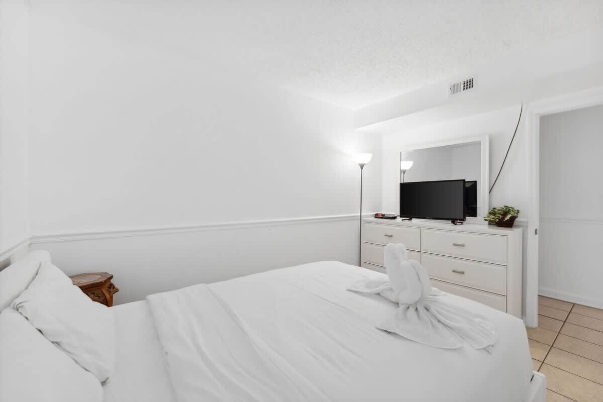 Ein Hotelzimmer mit einem Bett, einem Schminktisch mit Spiegel, einem Fernseher und einer kleinen Pflanze.
