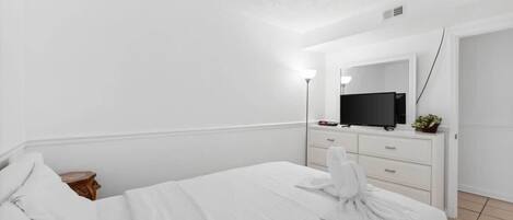 Ein Hotelzimmer mit einem Bett, einem Schminktisch mit Spiegel, einem Fernseher und einer kleinen Pflanze.