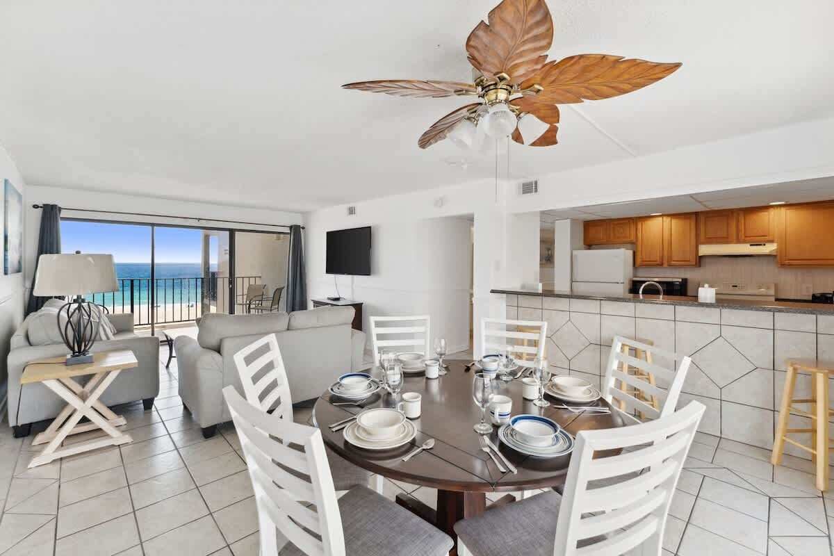 A modern dining area with a round table set for six, white chairs, and a ceiling fan with a leaf design.