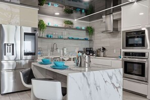 A modern kitchen with stainless steel appliances, a marble island, and teal accents. - The Summit 231 - Corner of Paradise (Panama City)