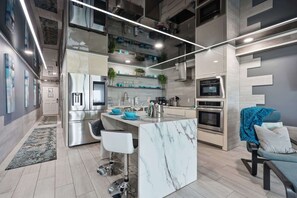 A modern kitchen with stainless steel appliances, a marble island, and a seating area with a blue chair and cushions. - The Summit 231 - Corner of Paradise (Panama City)