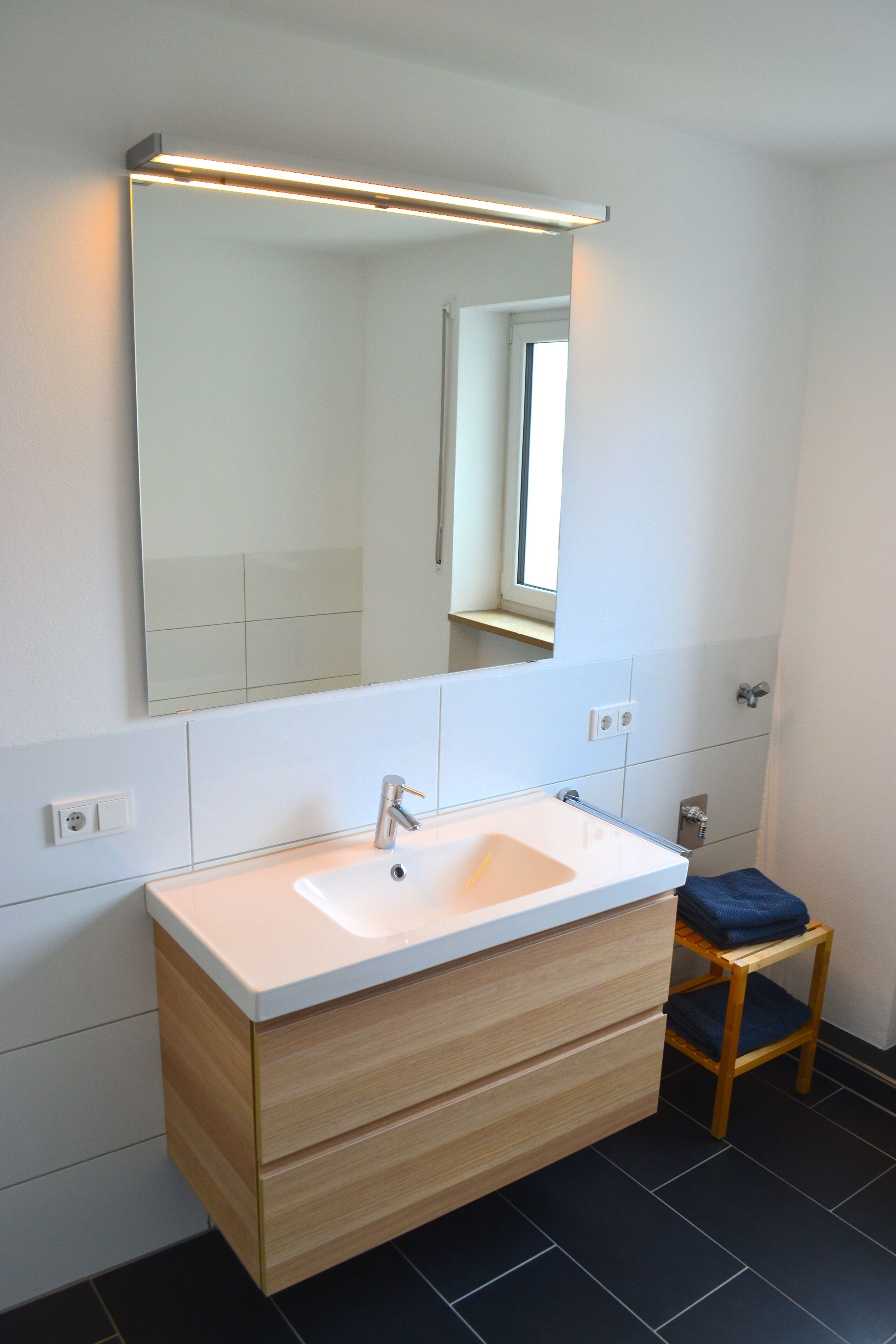 Un baño moderno con un lavamanos blanco, tocador de madera y un espejo encima.