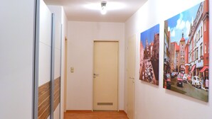 Un couloir au sol en bois, une porte au fond et deux tableaux accrochés aux murs.