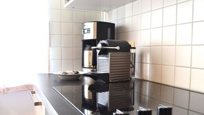 Une cuisine avec un plan de travail noir, une machine à café, un grille-pain et un bol de céréales.