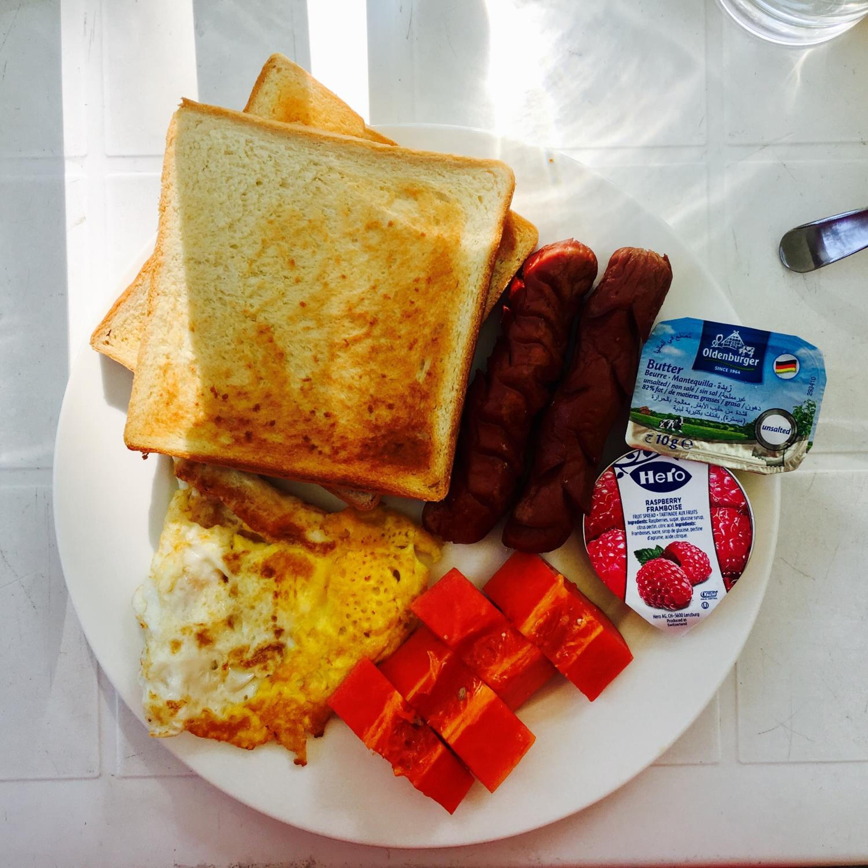 Een bord met toast, worstjes, roerei en een bakje frambozen.