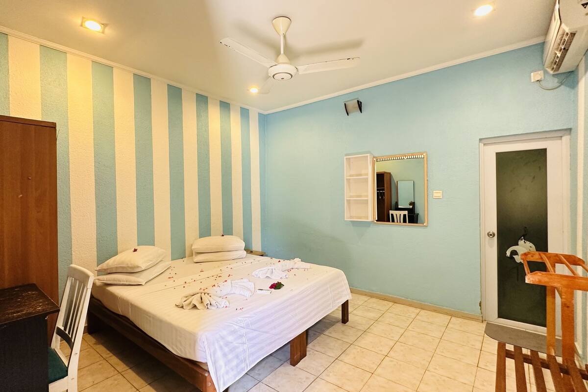 A hotel room with a bed, a desk, a chair, a wardrobe, a mirror, and a door.