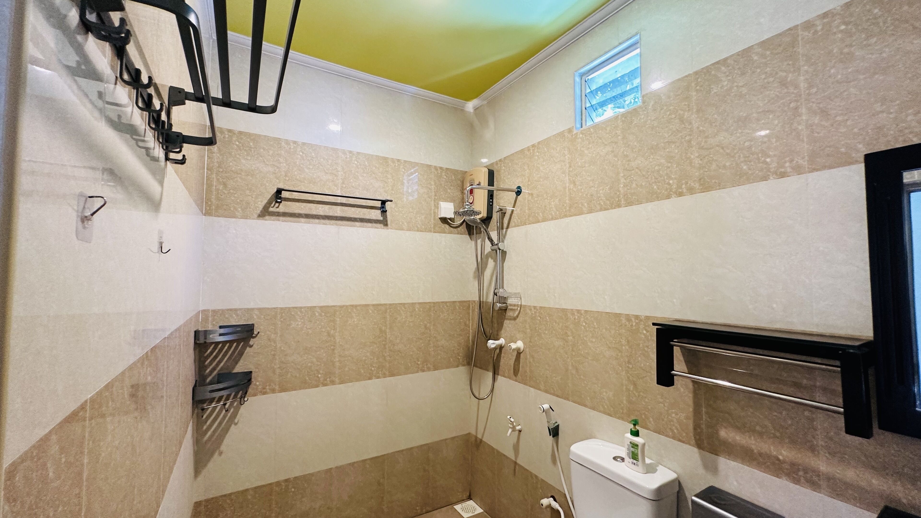 A small, tiled bathroom with a shower, toilet, and towel rack.