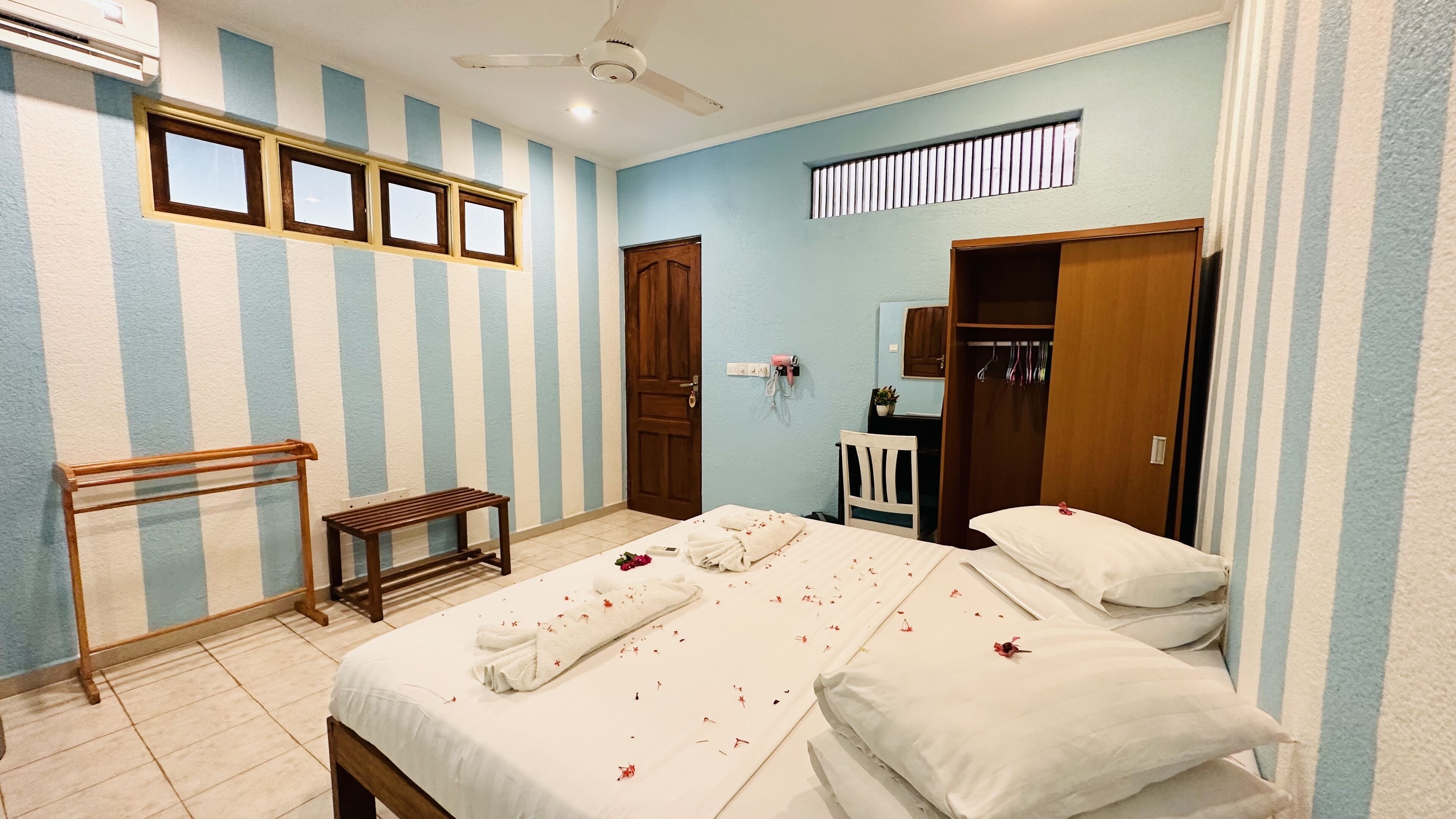 A hotel room with a bed, a bench, a wardrobe, and a ceiling fan.