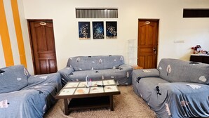 A living room with two grey sofas, a coffee table, and a small TV. There are three framed artworks on the wall and a wooden door with a number plate. - Midsummer Thulusdhoo (Thulusdhoo Island)