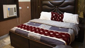 Un lit bien fait, avec une couvre-lit à motifs, une tête de lit sombre et un climatiseur fixé au mur.