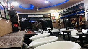 Un bar avec un long comptoir, de nombreux tabourets et un ventilateur de plafond.