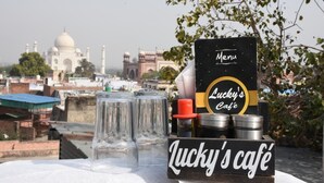 Une table dressée avec un menu et des verres, le tout mis en valeur par le Taj Mahal et un fort moghol en arrière-plan.