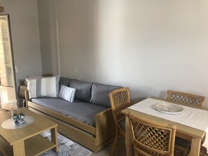 A compact living space with a sofa, a dining table, and two wicker chairs.