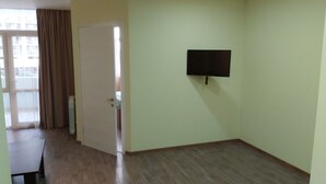 A room with a wooden floor, a flat-screen TV mounted on the wall, and a door leading to another room. - Good apartment 300 m from Black sea (Batumi)