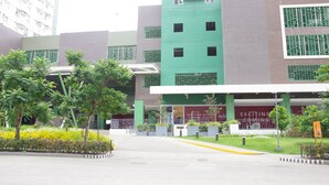 A multi-story building with a green and grey facade, a covered entrance, and a landscaped area with trees and plants. - Avida Towers Riala (Cebu City)