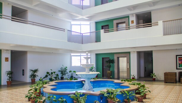 A spacious atrium with a central fountain surrounded by potted plants, multiple floors with balconies, and a tiled floor. - Spianada Residences (Cebu City)