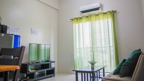 A living room with a flat-screen TV on a stand, a sofa, a coffee table, and a window with sheer curtains. - Spianada Residences (Cebu City)