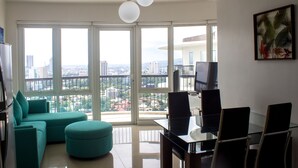 Een moderne woonkamer met een blauwgroene bank, een glazen eettafel en een stadszicht door grote ramen.