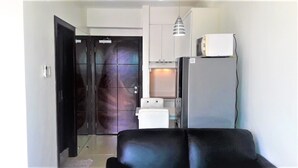 A compact living space with a black sofa, a white refrigerator, a water dispenser, and a door with a frosted glass panel. - City Suites Ramos Tower (Cebu City)