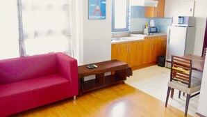 A modern living room with a red sofa, a wooden coffee table, and a dining area with a wooden chair and a small table. - City Suites Ramos Tower (Cebu City)