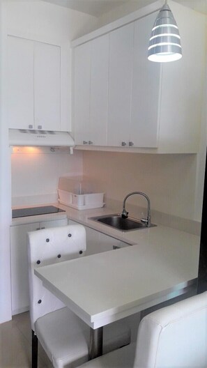 Una cocina compacta con armarios blancos, estufa integrada, un lavamanos y una zona de comedor con un banco.