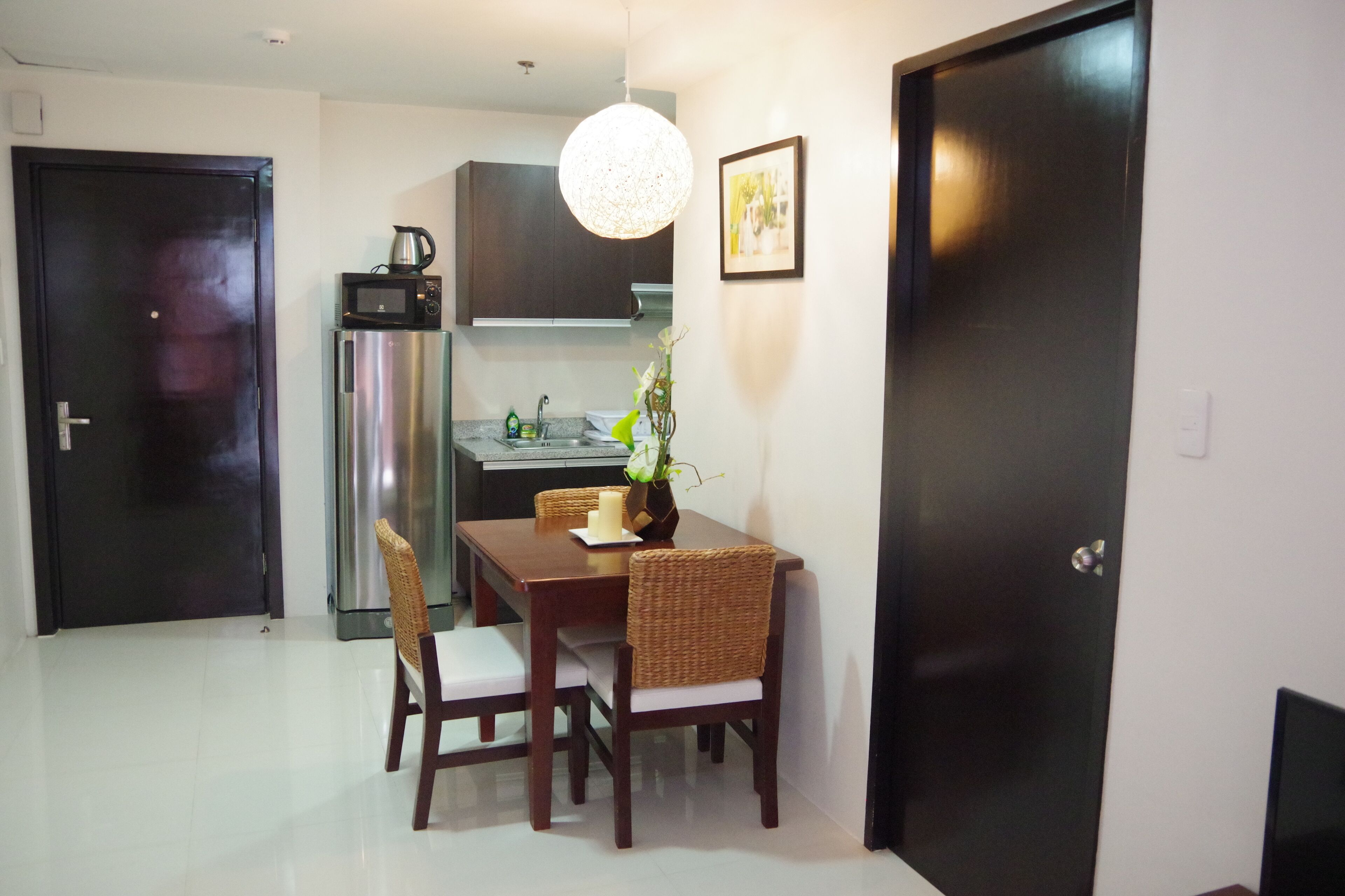 A compact kitchen with a microwave, stove, and sink. There is a dining table with chairs and a vase with flowers.
