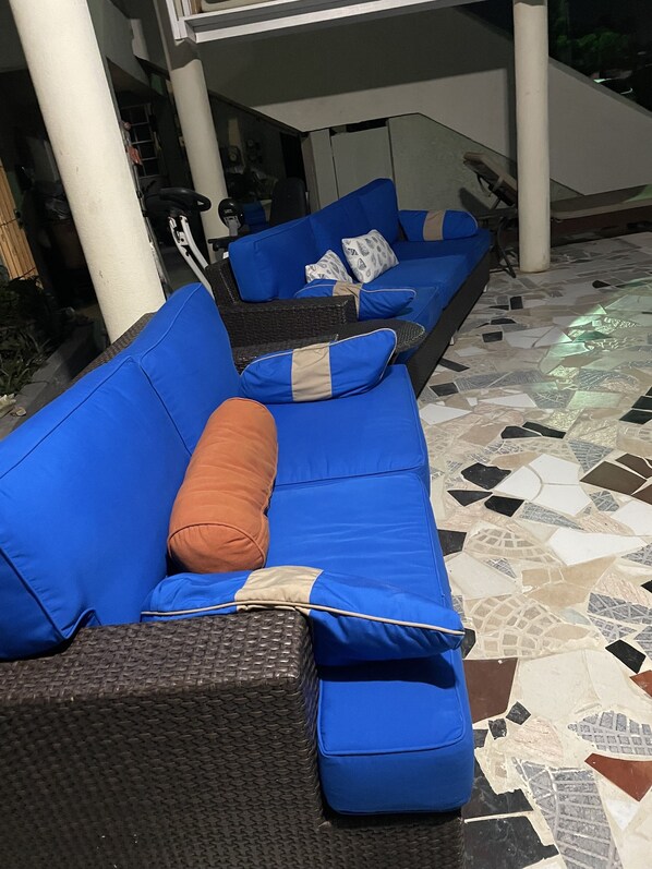 Un sofá azul con cojines, una silla de mimbre y un suelo de baldosas.