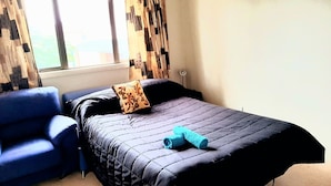 Ein Schlafzimmer mit einem Bett, einem blauen Sessel und einem Fenster mit Vorhängen.
