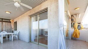 Une terrasse extérieure moderne, dotée d’une porte vitrée donnant sur un espace intérieur, de chaises en plastique blanches et d’un ventilateur de plafond.