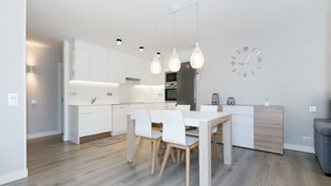Eine moderne Küche mit weißen Schränken, einem Esstisch mit Stühlen, Pendelleuchten und einer Wanduhr.