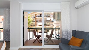Ein modernes Wohnzimmer mit einem grauen Sofa, einem Holzstuhl und einem Balkon mit Glastür.