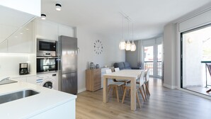 Eine moderne Küche mit integrierten Geräten, ein Essbereich mit Holztisch und Stühlen sowie ein großes Fenster mit Blick ins Freie.