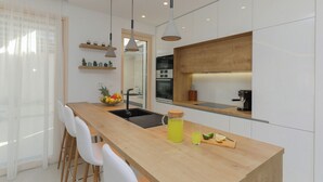A modern kitchen with a wooden countertop, white cabinets, and a built-in oven. There is a fruit bowl on the counter and a coffee machine. - Newly Built 5 Star Luxury Villa Bondi for 8 people Next to Beautiful Beach (Supetar)
