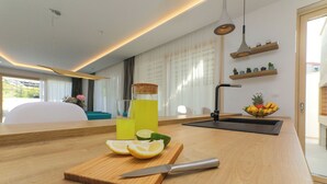 A modern kitchen with a wooden countertop, a cutting board with a knife, a glass of yellow drink, and a bowl of fruit. - Newly Built 5 Star Luxury Villa Bondi for 8 people Next to Beautiful Beach (Supetar)