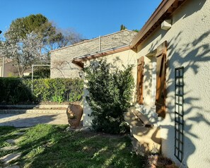A house with a stone facade, wooden shutters, and a small garden with a potted plant and grass.